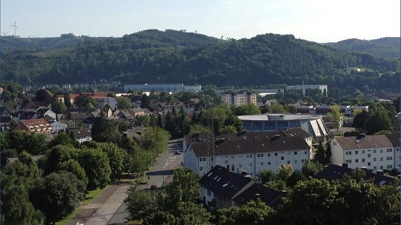 Einige Häusergruppen mit bergigen Waldabschnitten im Hintergrund.  