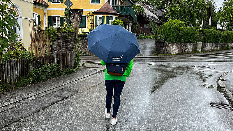 Auf dem Bild ist eine Person zu sehen, die mit einem Regenschirm durch einen Ort in Bayern läuft.