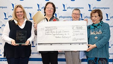 Vier Personen halten einen großen Scheck in der Hand und schauen in die Kamera. 