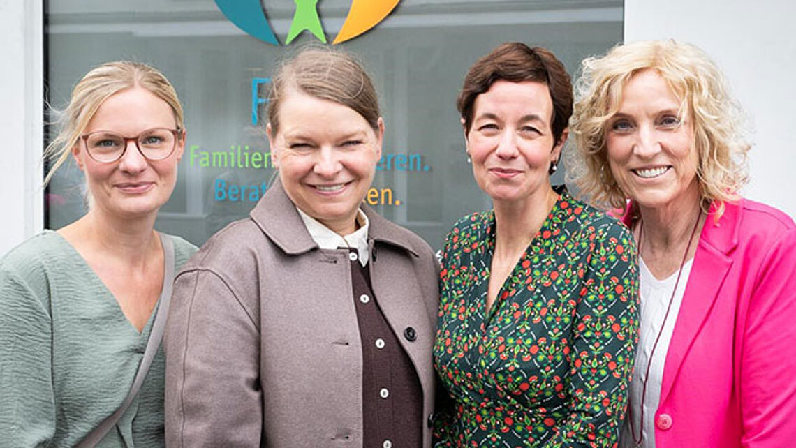 Vier Frauen stehen lachend vor einem mit Fenster, auf dem das FIBS-Logo klebt.