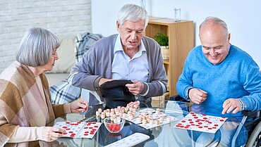 Drei ältere Menschen sitzen an einem Tisch und beschäftigen sich mit einem Spiel. 
