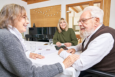 Zwei ältere Menschen sitzen mit einer Pflegeberaterin am Tisch.