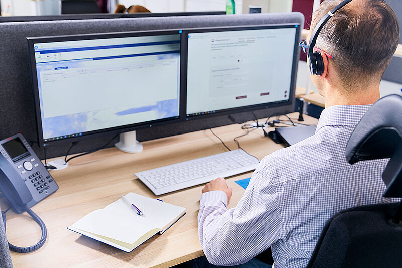 Ein Mann schaut auf zwei Bildschirme und trägt ein Headset. 