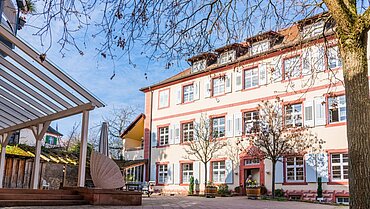 Ein älteres Gebäude, im Vordergrund ein Baum. 