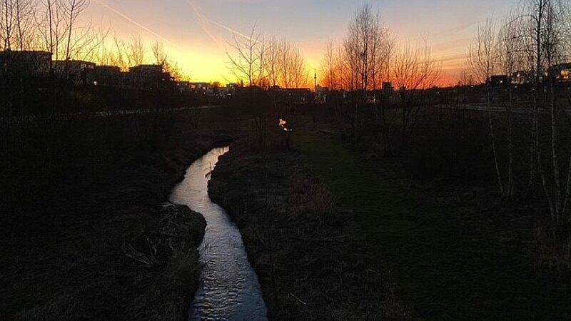 Vorne ist ein Flusslauf, der sich nach hinten schlängelt und in einem rot-gelben Sonnenuntergang verschwindet.   