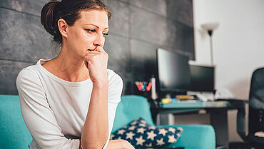 Frau auf Sofa sitzend, schaut nachdenklich.