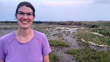 Eine Frau in einem lila T-Shirt steht vor einer Landschaft.
