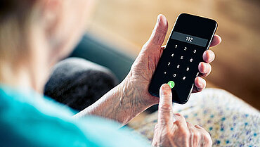 Eine alte Frau wählt auf einem Smartphone die Notrufnummer 112