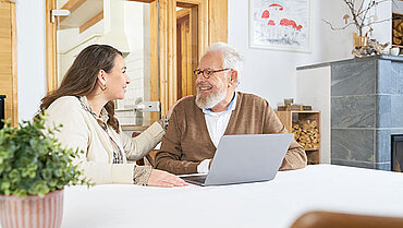 Ein Senior und seine Tochter sitzen gemeinsam am Computer und melden sich für den Newsletter von pflegeberatung.de an.