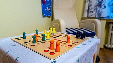 Eindruck aus der Tagespflege: Ein Sessel und ein kleiner Beistelltisch mit einem Mensch-Ärgere-dich-nicht-Spiel.