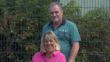 Auf dem Bild sind Rainer Seepe und Marion Kuehn-Seepe zu sehen. Rainer Seepe steht hinter seiner Frau und schiebt ihren Rollstuhl.