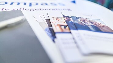 Flyer liegen aufgefächert auf einem Tisch, auf dem ein compass-Logo abgedruckt ist.
