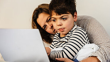 Eine Mutter sitzt mit ihrem behinderten Kind vor einem Laptop. 