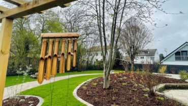 Das Bild zeigt den Sinnesgarten der Tagespflege. Im Vordergrund ist ein Glockenspiel zu sehen, ein gepflegter Garten im Hintergrund.