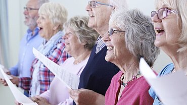 Ältere Menschen mit Notenblättern singen in einem Chor.