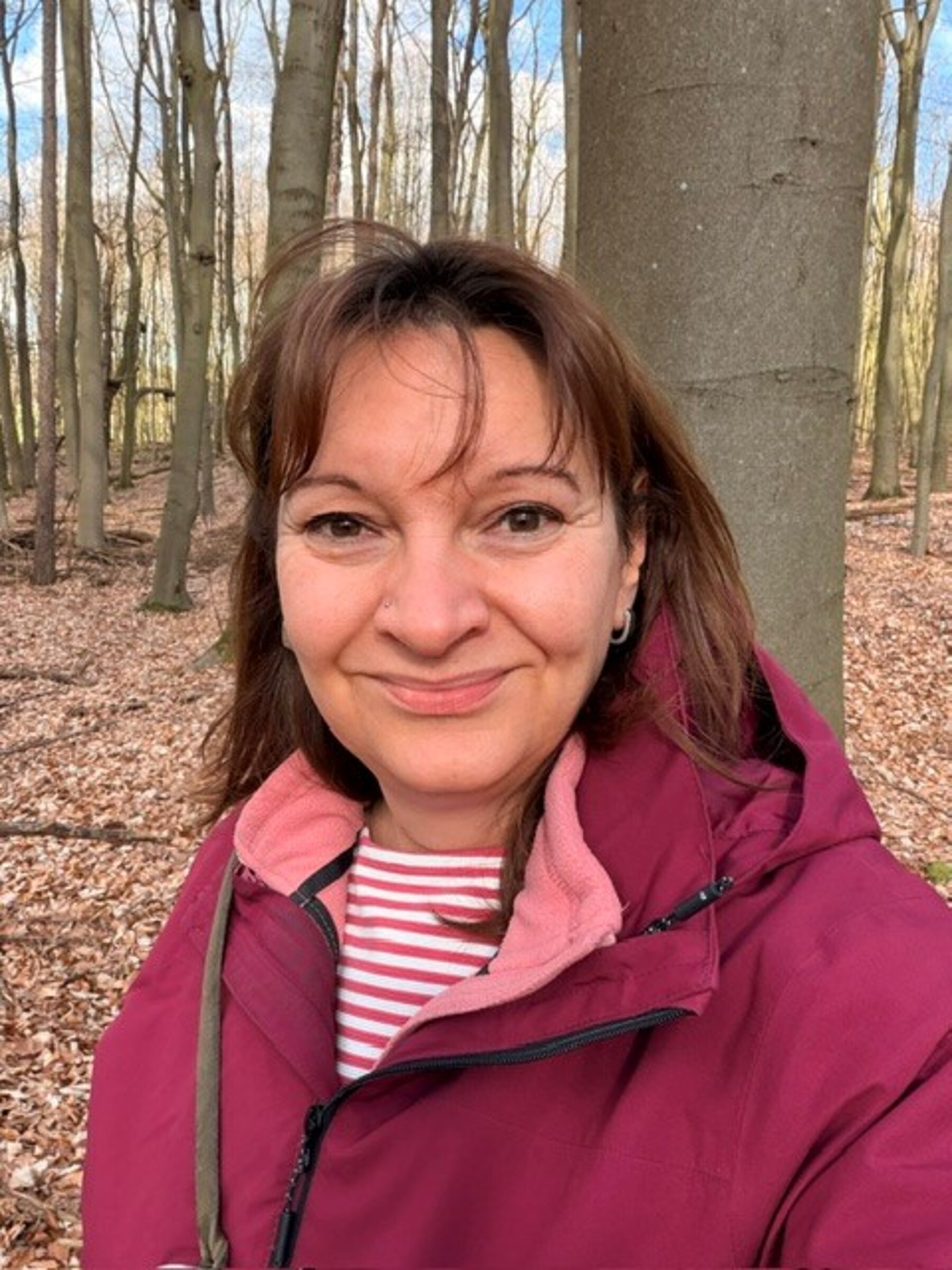 Eine Frau in roter Jacke, die in die Kamera blickt. 