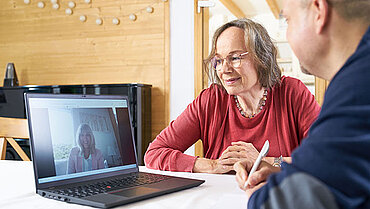 Ein Mann mit Notizblock und Kugelschreiber und eine Frau sitzen vor einem geöffneten Laptop.