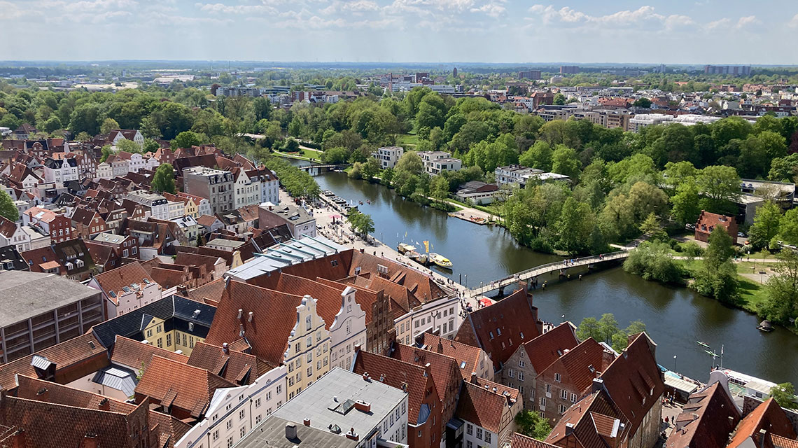 Blick von oben auf die Dächer von Lübeck mit Fluss und Grünstreifen im Hintergrund. 