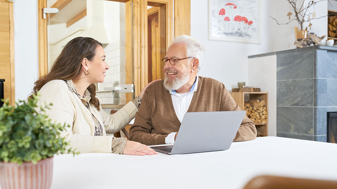 Ein Senior und seine Tochter sitzen gemeinsam am Computer und melden sich für den Newsletter von pflegeberatung.de an.