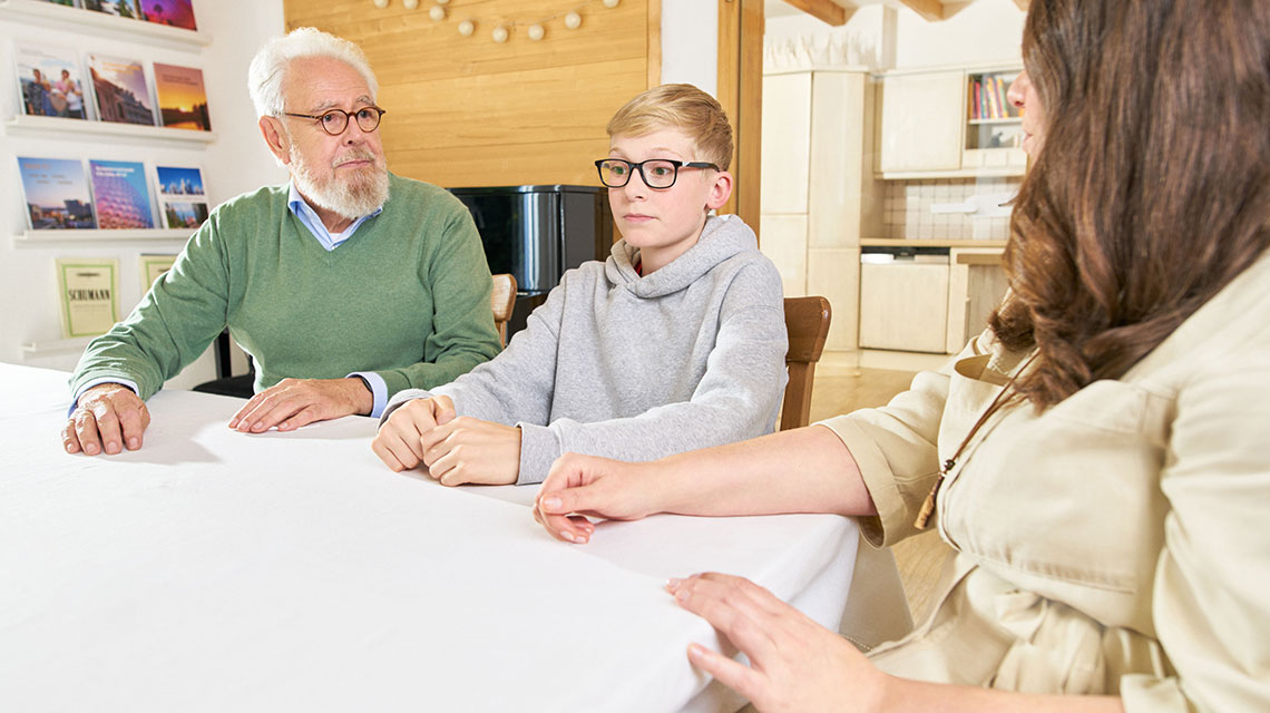 Ein Junge sitzt mit seinen Eltern am Küchentisch.