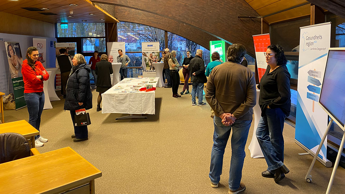 Mehrere Menschen stehen in einem Raum mit Ausstellbannern und unterhalten sich.