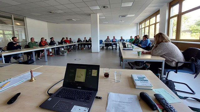 Bild zeigt eine Konferenzsituation, im Vordergrund Laptop und im Hintergrund Menschen