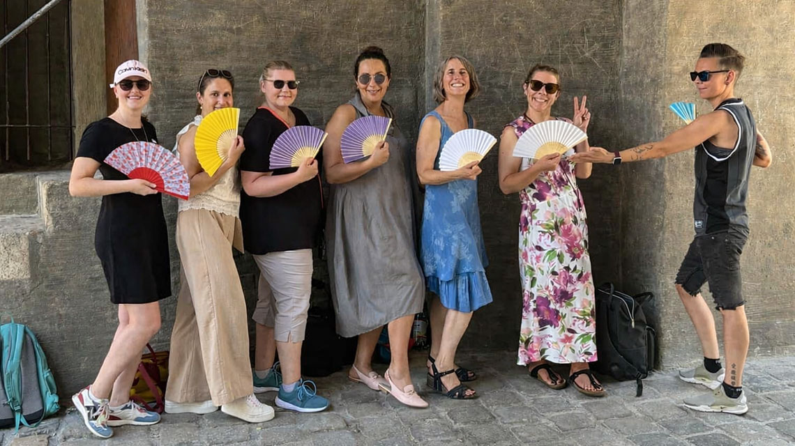 Sieben Personen nebeneinander auf einem Gruppenfoto mit Fächern in der Hand.